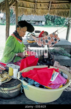 An elderly Miccosukee Indian woman cuts bright cloth to sew into traditional clothing at her Seminole tribal village in The Everglades in Florida,USA. Stock Photo