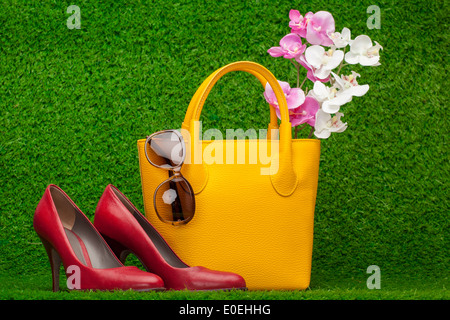 sunglasses, handbag and red shoes on green grass Stock Photo