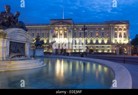 Buckingham Palace at night with Victoria Memorial statues reflected in water of fountain London England UK Stock Photo