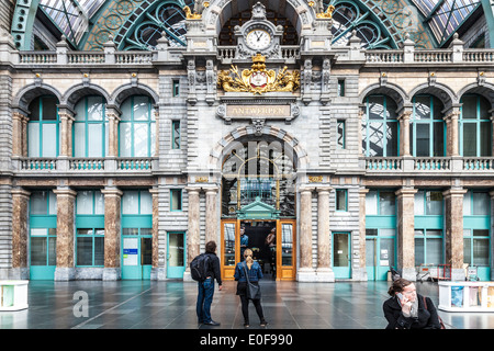 Young couple looks at the clock above the entrance hall of the Antwerpen-Centraal railway station. Stock Photo