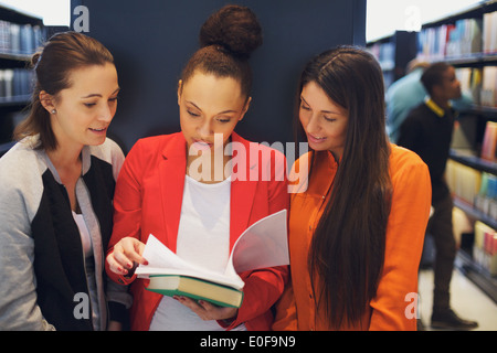 Multiethnic young students reading a book in library. Standing in public library sharing reference book for their studies. Stock Photo