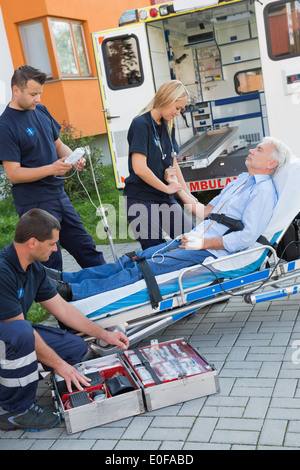 Paramedic team assisting injured senior man lying on stretcher outdoors Stock Photo