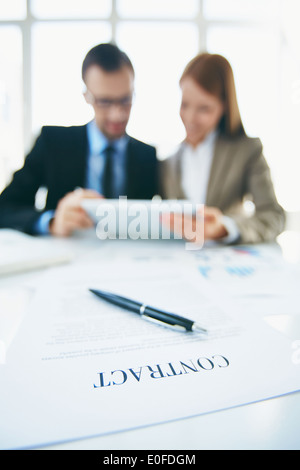 Image of business contract on workplace with two colleagues using touchpad on background Stock Photo