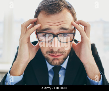 Frustrated businessman in eyeglasses touching his head Stock Photo