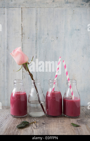 Blueberry & Blackcurrent Smoothies in milk bottles with stripy straws and a rose Stock Photo