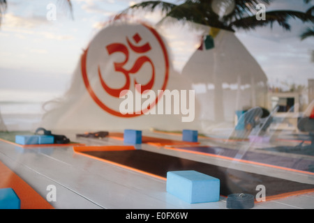 View of empty yoga studio with yoga mats and yoga blocks with Om symbol painted in orange on the wall with palm tree reflections Stock Photo