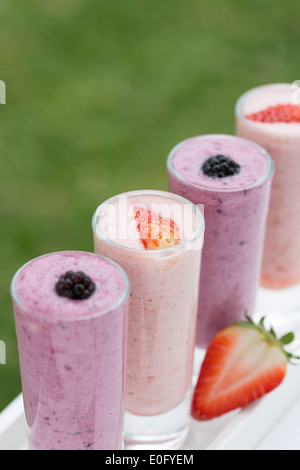 Strawberry and blackberry drinks in summer garden, served in tall shot glasses on white table Stock Photo