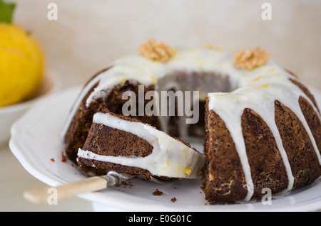 Round mould iced date and walnut cake served on white plate, with lemons in background Stock Photo