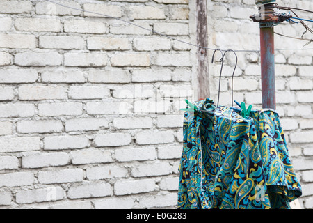 Blue and green patterned shirt on a wire clothesline in front of a white brick wall. Stock Photo