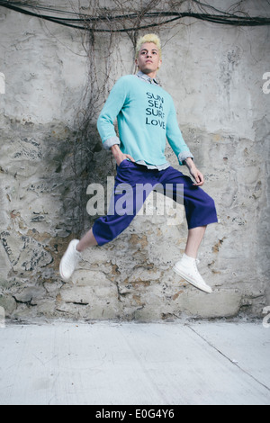 Young man in an urban setting, dreaming of the beach and wanting to go there, 'Sun, Sea, Surf, Love' printed on the sweater. Stock Photo