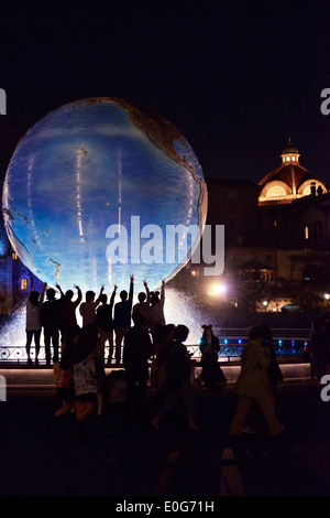 Children posing for a photo at Earth globe fountain at night in Tokyo Disney restort Disneysea theme park, Japan Stock Photo