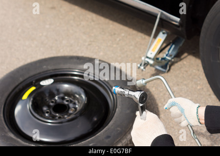 Close up view of the gloved hands of a mechanic changing a car tyre holding a wheel spanner and torque wrench above the spare Stock Photo