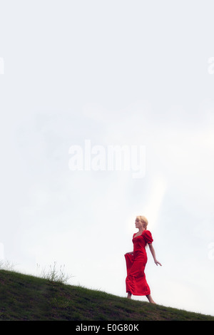 a woman in a red dress is walking uphill Stock Photo