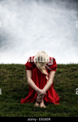a woman in a red dress is sitting on a hill Stock Photo