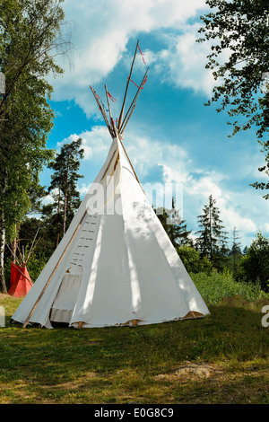 A tipi (also tepee and teepee) is a conical tent, traditionally made of animal skins, and wooden poles against blue sky Stock Photo