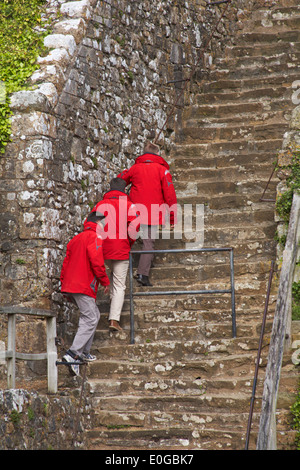 follow the leader concept - three men in red jackets climb the steps at Carisbrooke Castle, Carisbrooke, Newport, Isle of Wight, Hampshire UK in May Stock Photo