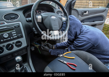 A man wearing a hoody hot wiring a car. Stock Photo