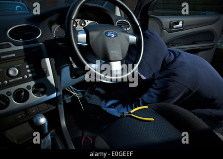 A man wearing a hoody hot wiring a car. Stock Photo