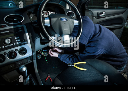 A man wearing a hoody hot wiring a car. Stock Photo
