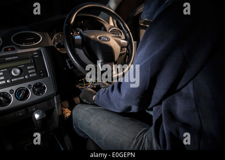 A man wearing a hoody hot wiring a car. Stock Photo