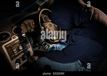 A man wearing a hoody hot wiring a car. Stock Photo