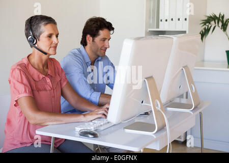 Casual business team working at desk using computers with woman using headset Stock Photo