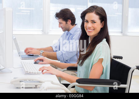 Worker in wheelchair working on computer smiles to camera Stock Photo
