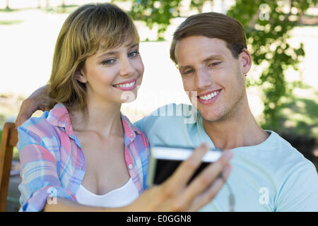 Cute couple sitting on bench in the park taking a selfie Stock Photo