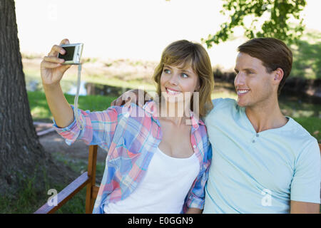 Cute couple sitting on bench in the park taking a selfie Stock Photo