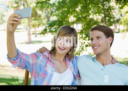 Cute couple sitting on bench in the park taking a selfie Stock Photo