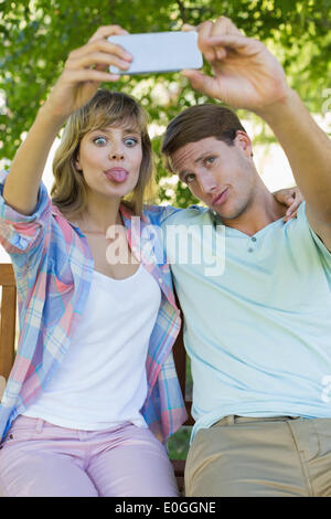 Funny couple sitting on bench in the park taking a selfie Stock Photo