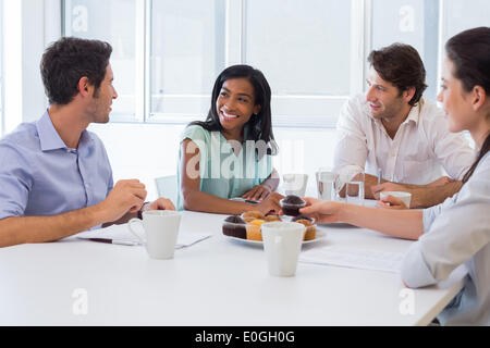 Work colleagues chatting in board room while enjoying coffee and muffins Stock Photo