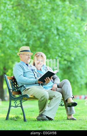 Mature couple reading a book seated on bench in park Stock Photo