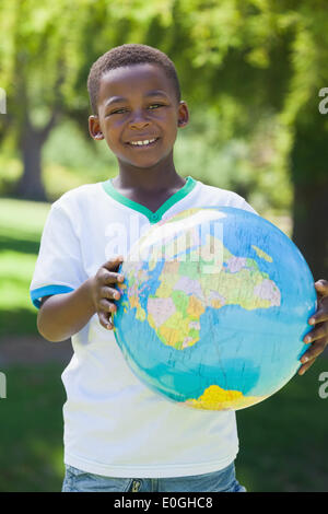 Little boy smiling at camera holding globe in the park Stock Photo