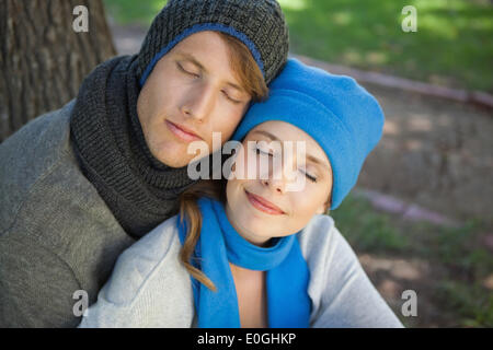 Cute couple sitting and embracing in the park with eyes closed Stock Photo