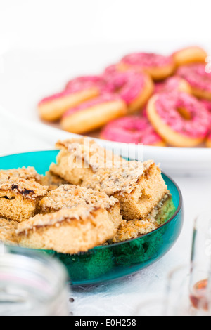 Closeup of slices of dry cake in glass serving bowl with pink colored donuts in bowl in background Stock Photo