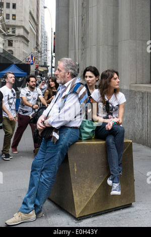 tourist family sit resting on bronze bollard protecting top of Wall street at Broadway in Lower Manhattan from vehicular access Stock Photo