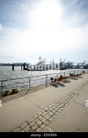 People in deck chairs watching towing boats at Neumuehlen pier, Hamburg harbour, Germany Stock Photo