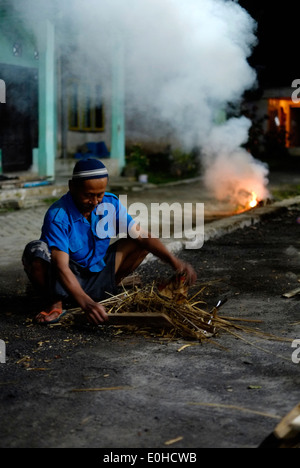 indonesian local villager working at night by the light of a single strip lamp fashioning bamboo and discarding the waste wood Stock Photo