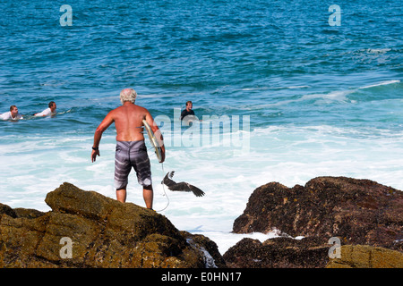 Senior adult male surfer stands on rocky shore waiting to jump into the water, surfing beach, Victoria Bay, Garden Route Stock Photo