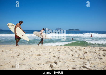 RIO DE JANEIRO, BRAZIL - FEBRUARY 20, 2014: Pair of young Brazilian surfers walk with surfboards along the shore Ipanema Beach. Stock Photo