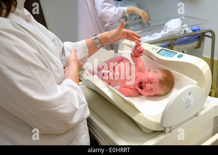 A crying baby girl is being weighed at the hospital after birth. Stock Photo