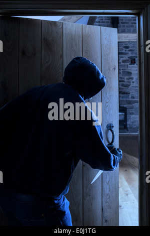 An anonymous hooded male carrying a knife entering a room. Stock Photo
