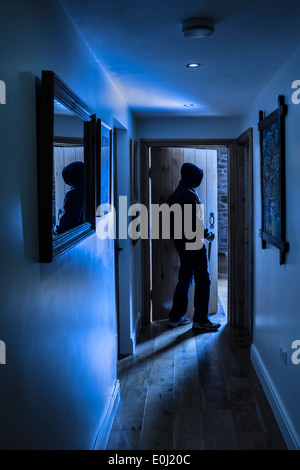 An anonymous hooded male carrying a knife entering a room carrying a knife. Stock Photo