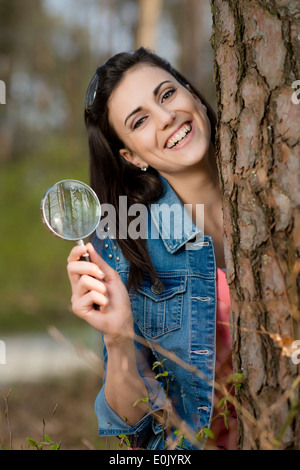 Young woman with magnifying glass next to tree trunk, (Model release) Stock Photo