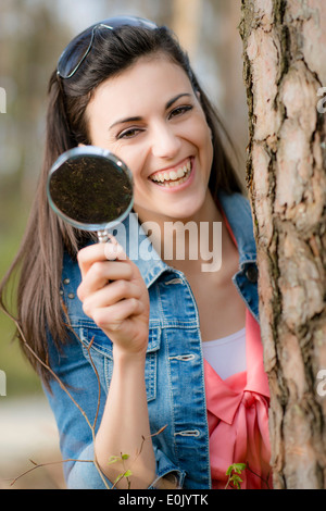 Young woman with magnifying glass next to tree trunk, (Model release) Stock Photo