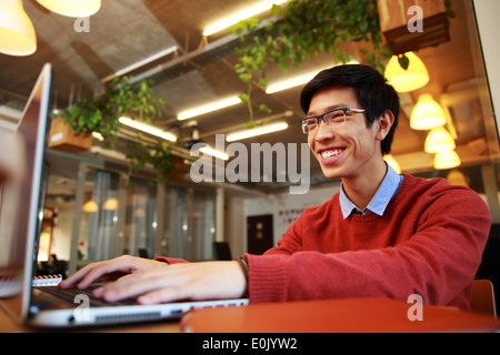 Cheerful asian man in glasses typing on laptop in office Stock Photo