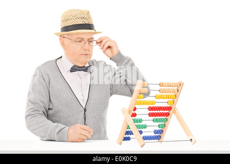 Senior man looking at an abacus seated at table Stock Photo