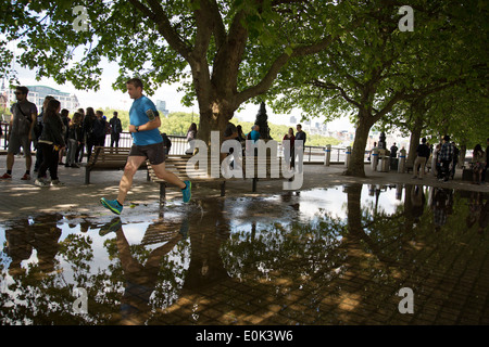 Man running through a deep puddle under trees after heavy rain on the riverside walkway. South Bank, London, UK. Stock Photo