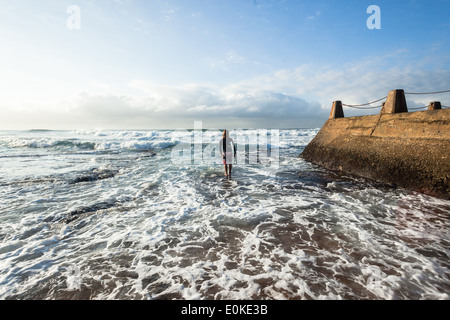 Surfing surfer unidentified on beach entering walking towards the ocean waves Stock Photo